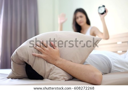 Lazy man use pillow close his ears and want to sleep . His wife would like husband wake up. Blur woman as background. Famlity concept.