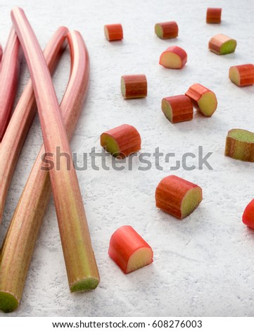 Fresh rhubarb and cut pieces of rhubarb on textured white marbled background. Shallow depth of field.