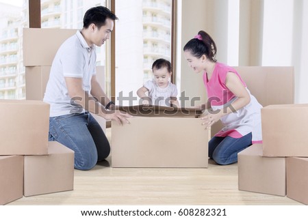Picture of young parents and child unpacking cardboard together while kneeling near the window