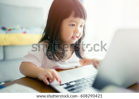 Portrait of a little girl watching laptop.Little asian girl with laptop computer or notebook in living rome at home.Learning concept.Shopping online concept.
