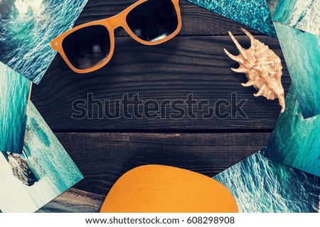 Sunglasses, shell, cap, and pictures with the image of the sea on a wooden surface. Top view