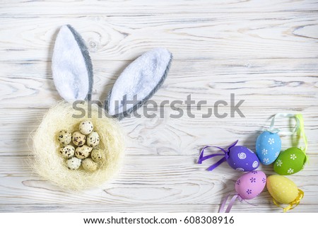 A nest with colored Easter eggs and bunny ears at home on Easter day. Celebrating Easter at spring. Painting eggs. Wooden background