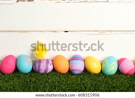 Colorful Easter Eggs in a Row on Grass against a Distressed White Wood  Board Wall Background with room or space for copy, text, or your words.  It's a horizontal with a Cute Baby Chick Singing.
