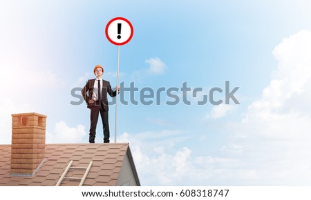 Young businessman with roadsign in hand standing on brick roof. Mixed media