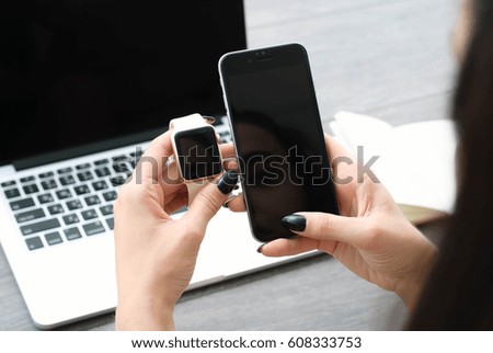 Female hand with smartwatch with holding mobile phone on laptop computer, View from above