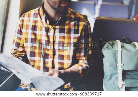 Enjoy travel. Young hipster smile man with backpack traveling by train sitting near window holding in hand and looking map. Tourist in summer shirt planing route of railway, railroad transport concept