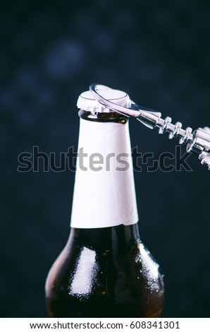 Glass bottle of cold beer and iron opener on a dark background. Hand opening a bottle. Alcohol and drinks concept. 