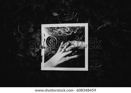 Black and white picture of wedding rings lying on photo of newlyweds hands