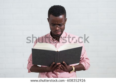 Happy afro man with book and glasses. Young african hipster guy in casual clothes on white wall background