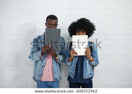 Cheerful young african student couple holding and reading a book together on white brick wall background