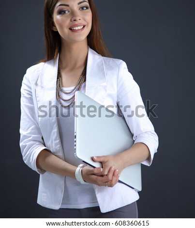 Young woman holding a laptop, standing on gray background