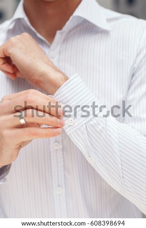 Man buttons cuff-link on French cuffs sleeves luxury white shirt. Close up of a businessman showing a shirt cuff.