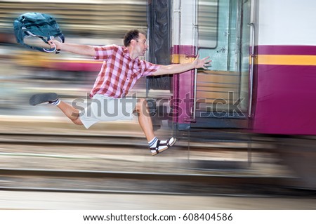 Tourist with bag running behind the train. A man runs for a moving wagon. Backpacker hurries for train departing from the station. Journey to the last minute. Royalty-Free Stock Photo #608404586