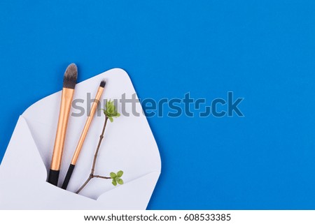 Make up brushes in white envelope with first spring gentle leaves and buds on small tree branch. Top view