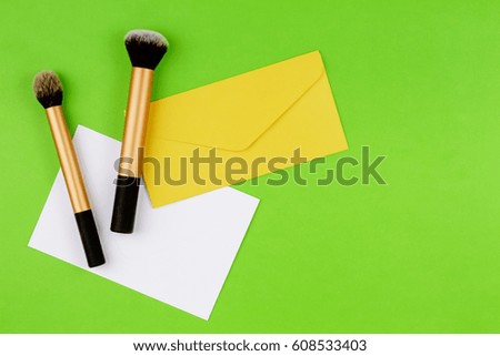 Make up brushes with yellow envelope and white blank card on greenery background. Top view. Flat lay.