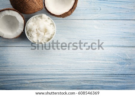 Coconuts and bowl with fresh oil on light wooden background