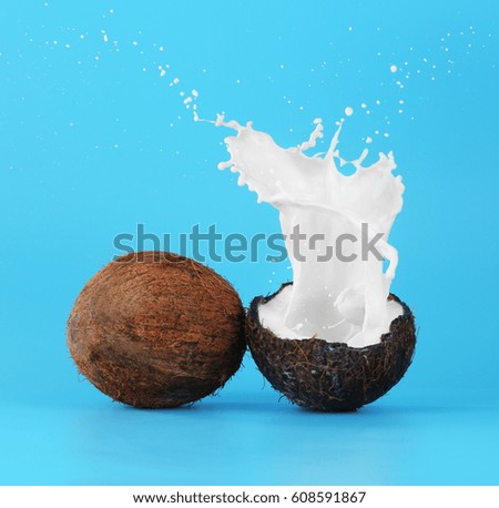 Coconuts with splashes of milk on color background