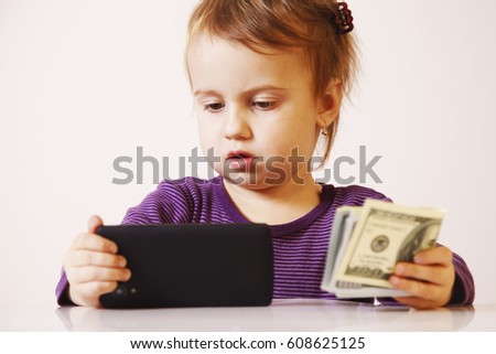 Successful business baby girl holding a smartphone in front of bunch of money (humorous picture)