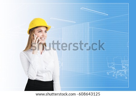 Portrait of a blond businesswoman in a yellow hardhat talking on her cell phone with a blueprint in the background.