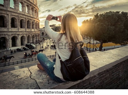 Woman tourist selfie with phone camera in hands near the Coliseum in Rome under sunlight and blue sky. Famous popular touristic place in the world.