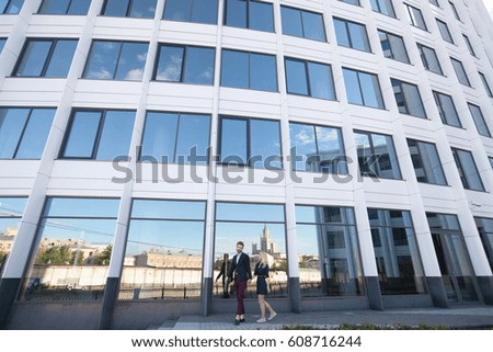 Man and woman walk hand against the glass of the building.