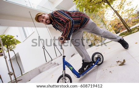 Happy playful adult man on scooter in front of his modern house