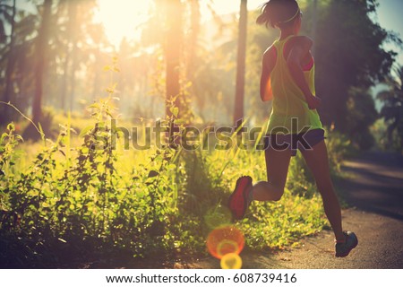 Young fitness woman running at morning tropical forest trail  Royalty-Free Stock Photo #608739416
