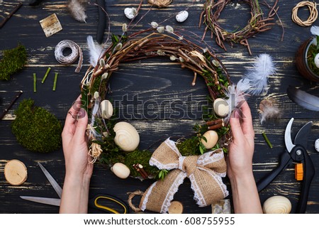 Female hands holding a handmade pussy willow wreath, flay lay picture. Pussy willow, feathers, green moss, twigs