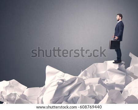Thoughtful young businessman standing on a pile of crumpled paper with a grey background