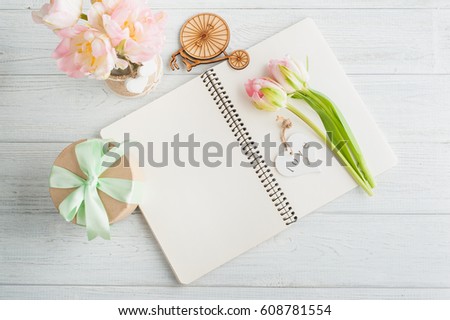 Overhead shot a bouquet of pink tulips and gift over white wood table top with an open journal. Flat lay top view style.