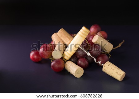 Many wine corks and a vintage cork screw and red grape on a dark background.