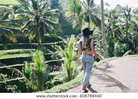 Young blonde hipster woman wearing black hat and jeans travelling around Asia, enjoying green rice terrace view, wanderlust blogger, Bali luxury vacation, taking pictures with her camera