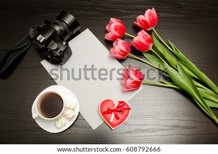 Clean sheet of paper, pink tulips, a camera and a mug of coffee. Black table. top view