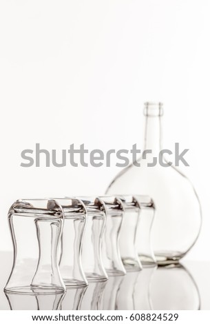 On a reflective tile is an empty transparent bottle and glass