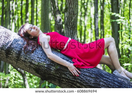 Girl in red dress on the tree in the morning forest