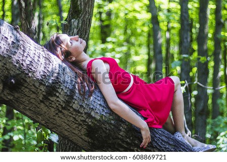 Girl in red dress on the tree in the morning forest