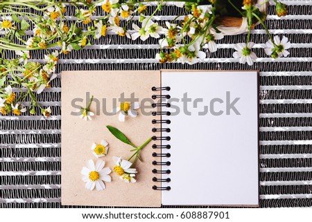 Blank notebook with white flower and bas ket of flower on steel net table View from above with copy space
