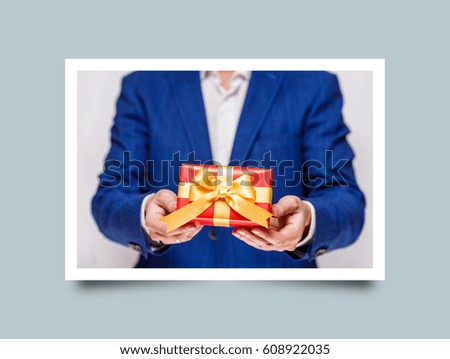 Male hands holding a gift box. Present wrapped with ribbon and bow. Christmas or birthday red package. Man in suit and white shirt. Photo frame design with shadow.