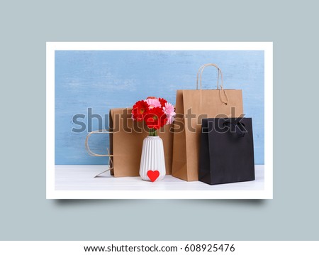 Mockup of blank shopping bags. Gerbera flowers and red heart. Brown and black craft packages. Concept for sales or discounts. Blue wooden rustic board. Photo frame design with shadow.