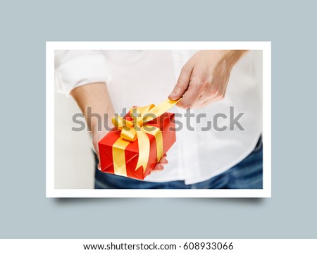 Male hands holding a gift box. Present wrapped with ribbon and bow. Christmas or birthday red package. Man in white shirt pulls the ribbon. Photo frame design with shadow.