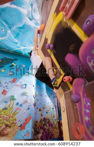 A little boy in a white T-shirt scrambles up on a children's climbing wall