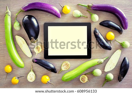Cooking and technology. Tablet computer with collection of fresh colorful eggplants on the wooden table. Top view.