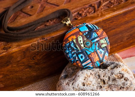 Boho abstract african pendant near wooden box. Artisan jewelry. Handmade jewelry from polymer clay. Unique mosaic necklace.Space for text advertising.