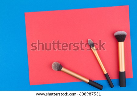Make up brushes with red blank paper on blue background. Top view. Flat lay. Copy space for text
