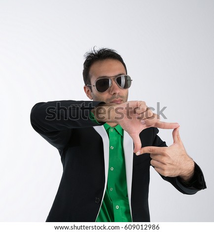 A young movie director showing a gesture with his fingers. In a black suit, green shirt and sunglasses