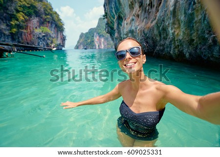 Traveling in Thailand. Pretty young woman in swimsuit taking selfie on the tropical beach.