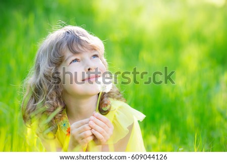 Happy child blowing dandelion flower outdoors. Girl having fun in spring park. Blurred green background. Dream and imagination concept