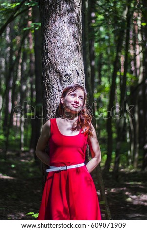 Girl in red dress hug the tree in green summer forest