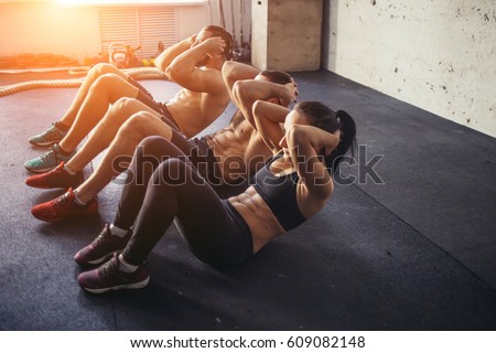 Group of athletic adult men and women performing sit up exercises to strengthen their core abdominal muscles at fitness training Royalty-Free Stock Photo #609082148