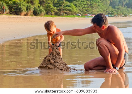 father and his little son building sand castle at beach 